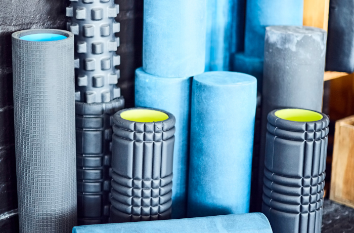 Various foam rollers of different sizes and textures stacked together, featuring a mix of blue and black designs for muscle recovery.