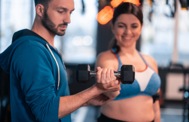 A personal trainer assisting a woman with dumbbell exercises,showcasing Wellfitsource's rehab and fitness equipment like resistance bands, dumbbells, and jump ropes.