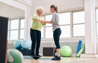 A therapist assisting an elderly woman with balance training using Wellfitsource's therapy accessories, including stability balls, balance trainers, and rehabilitation tools.