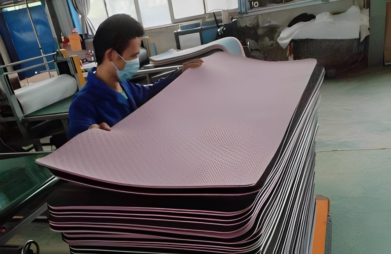A worker manually inspecting a stack of TPE yoga mats to ensure high-quality standards before packaging.