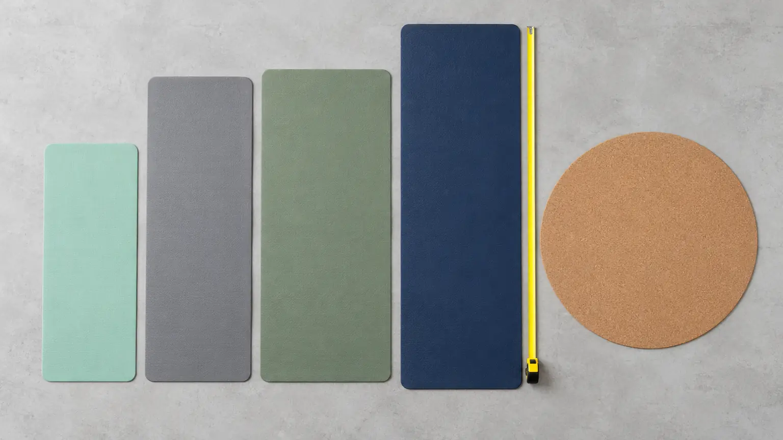 Five yoga mats of different lengths and widths laid flat beside a round mat and a tape measure