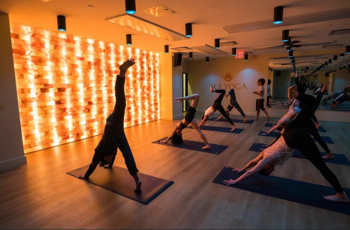 Hot yoga class with students practicing on PU yoga mats in a heated studio with glowing Himalayan salt wall.