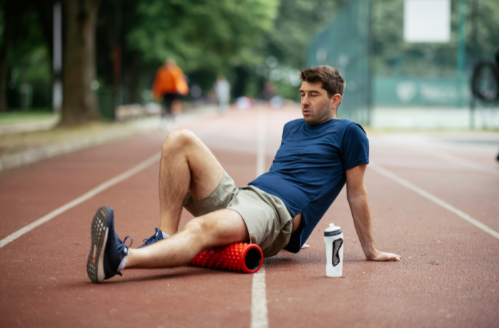Male athlete foam rolling legs on running track after cycling session