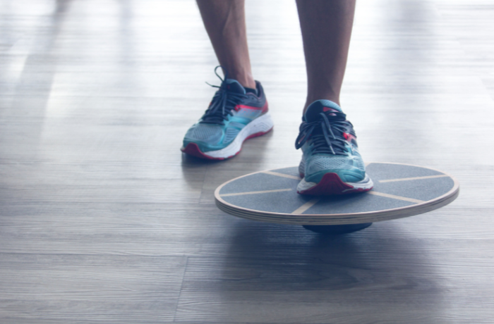 Person mit Sportschuhen beim Gleichgewichtstraining auf einem Balance Board
