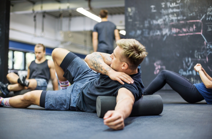 Man using black foam roller at gym for upper back release