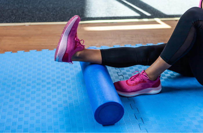 Feet resting on the end of a blue foam roller against a gym mat