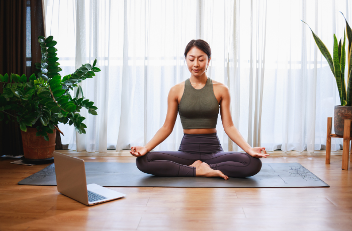 Woman meditating in lotus pose during a virtual yoga session

