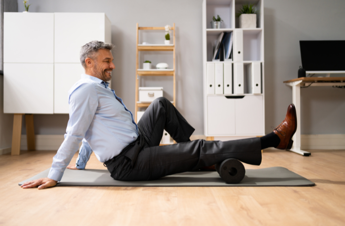 Middle-aged man in business attire rolling his calves on a black foam roller