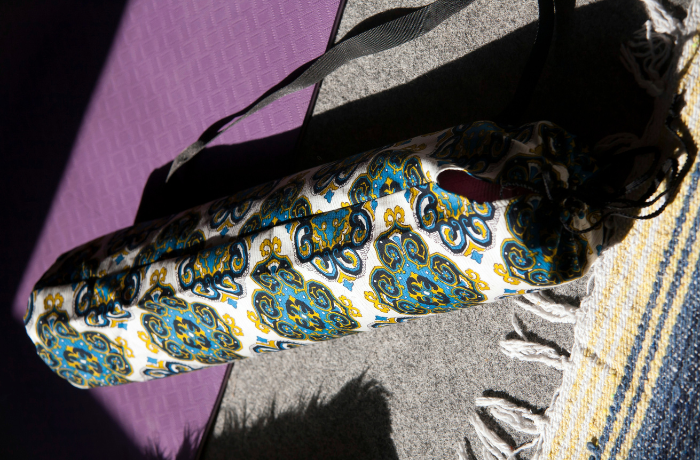 Patterned floral yoga mat bag resting on a purple mat indoors

