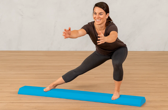 Woman balancing in side lunge atop a long narrow foam balance pad to train coordination and proprioception