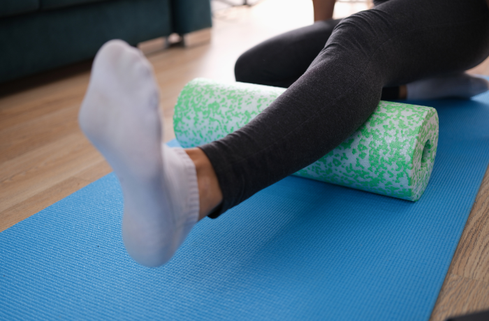 Close-up of a person foam rolling their calf with a soft, speckled EPE foam roller on a blue mat.