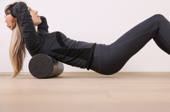 Woman lying back on a black textured foam roller under her thoracic spine performing self-myofascial release
