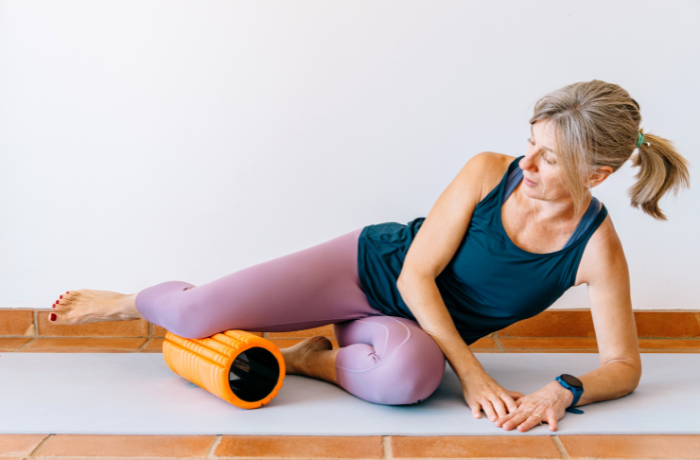 Senior woman rolling thigh with orange foam roller
