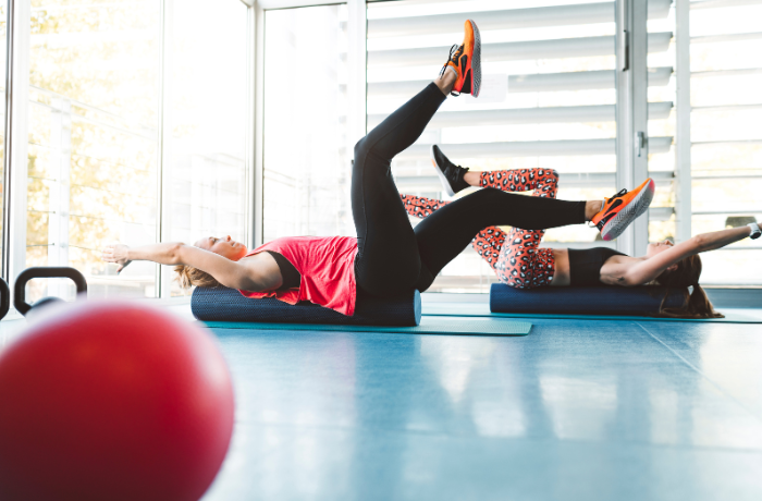 Two women exercising on foam rollers in fitness studio

