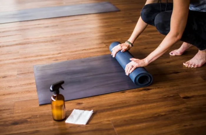 Woman rolling up a yoga mat after cleaning, next to a spray bottle and cloth.
