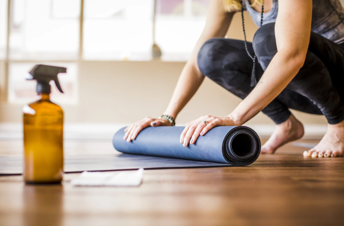 Yoga mat on a wooden floor with a spray bottle and cloth placed beside it.