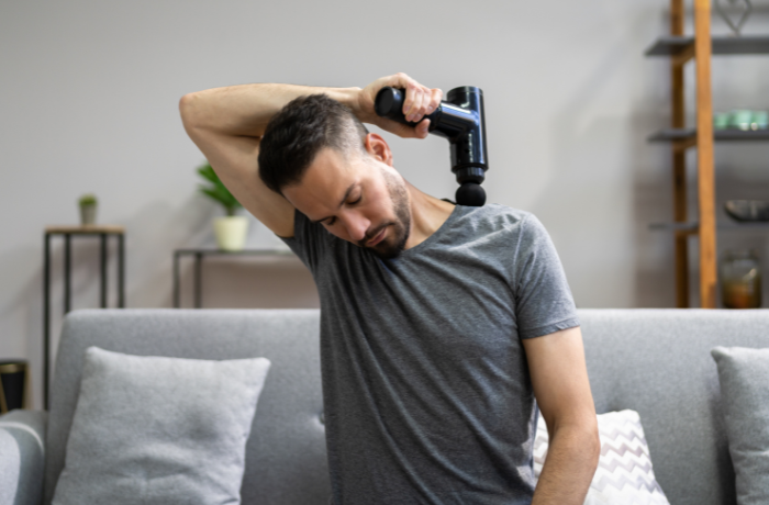 Man using massage gun on shoulder for home muscle recovery
