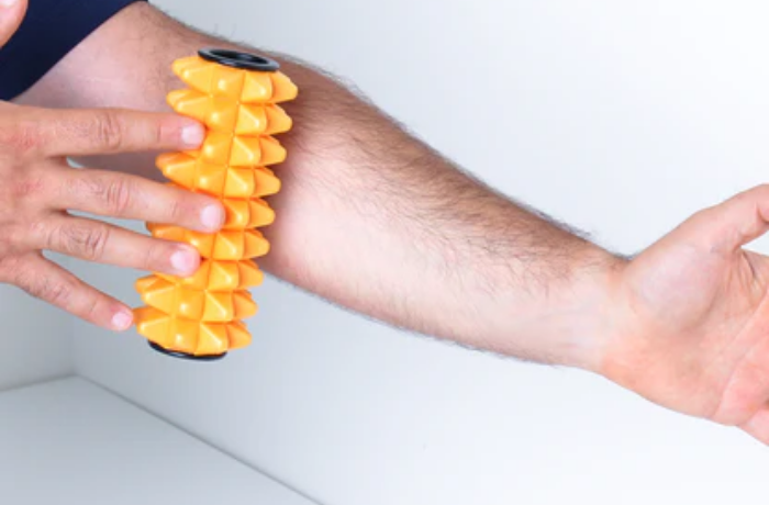 Man rolling orange mini massage roller on forearm for muscle tension release and improved blood flow.
